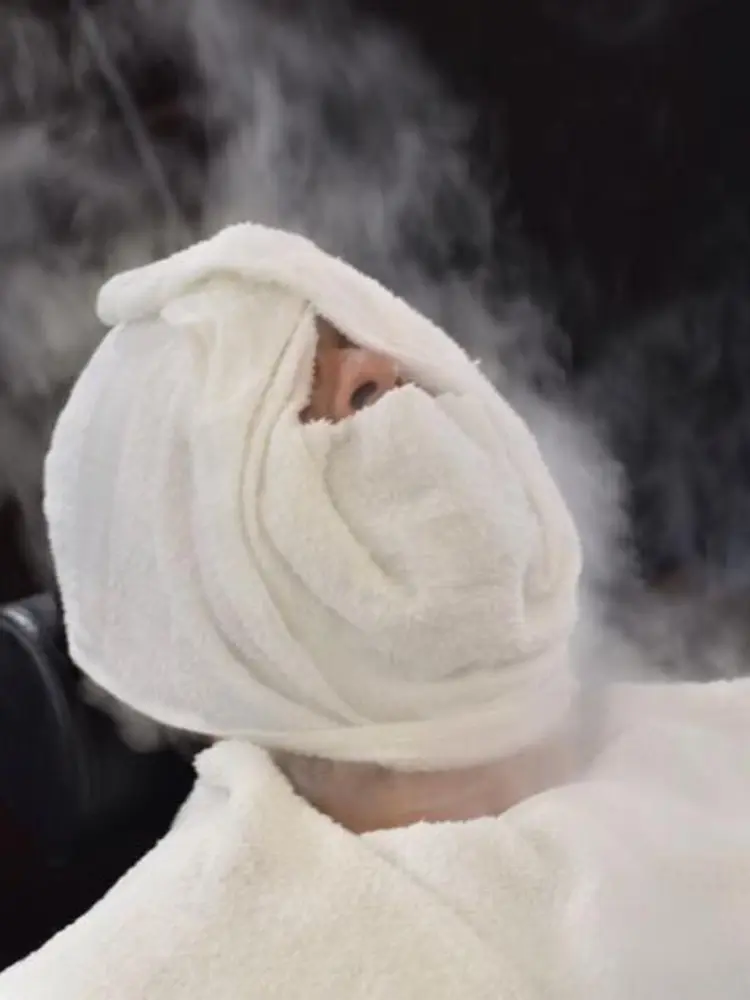 Client reclined in the chair with a steaming hot towel wrapped around the face