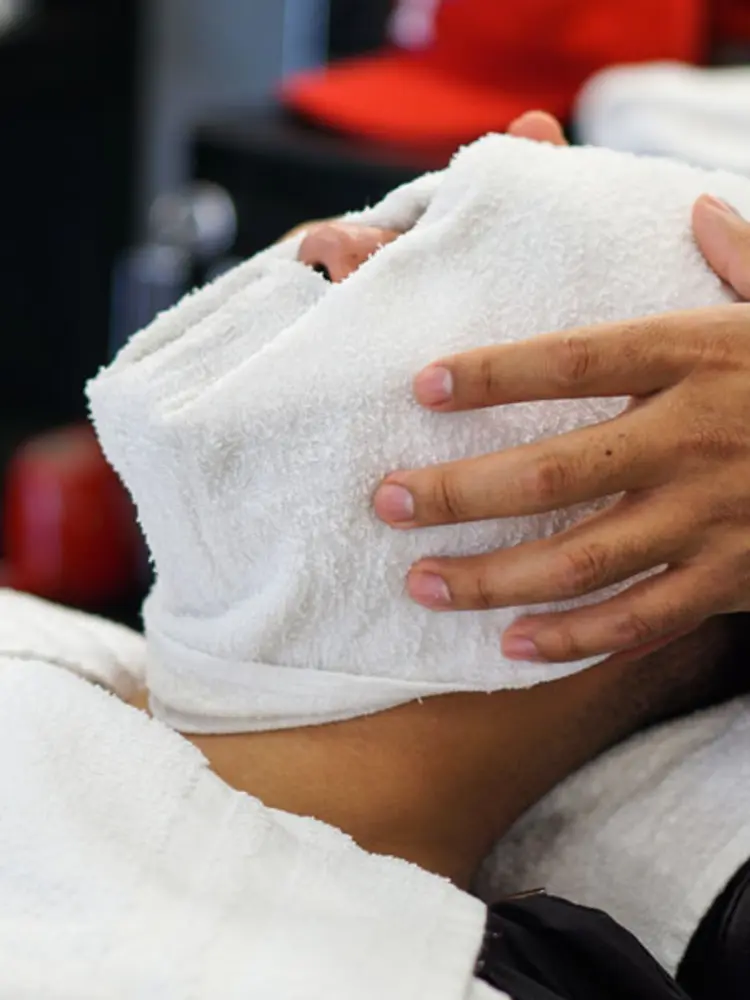 Barber pressing a warm white towel onto a client's face