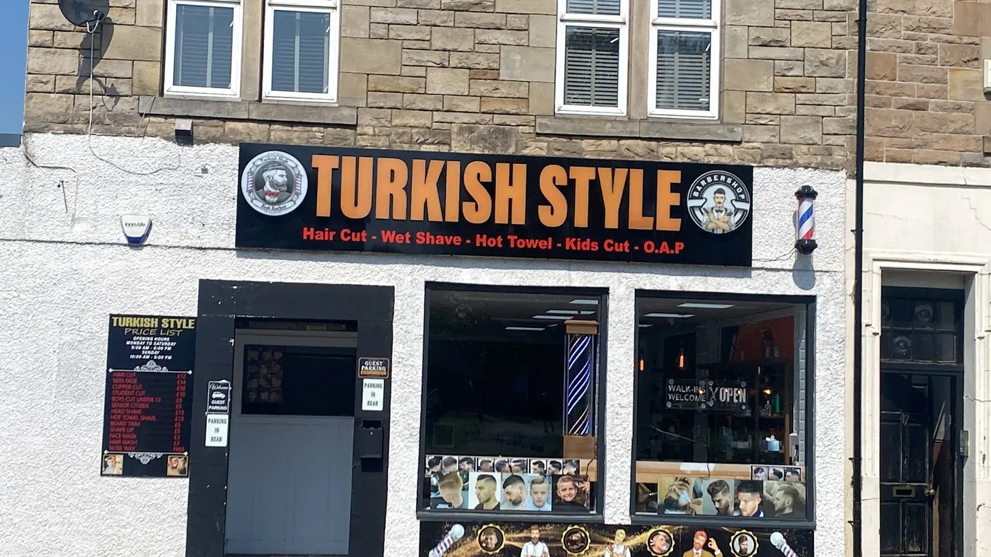 Turkish Style barbershop shopfront on Borestone Crescent with black and orange sign and barber poles