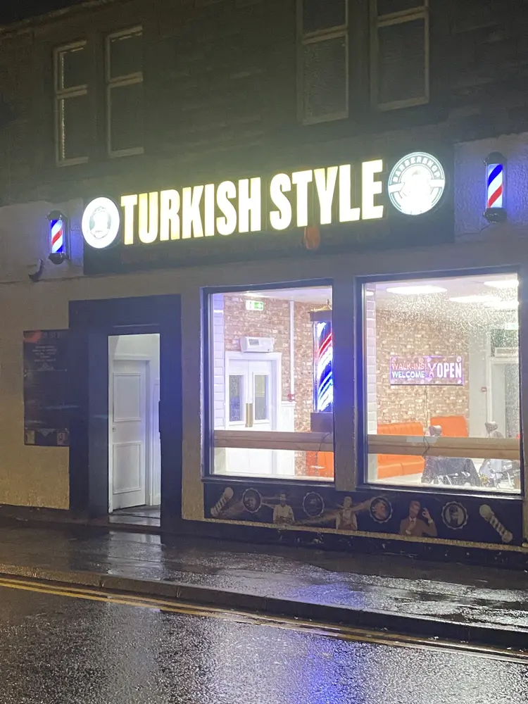 Turkish Style sign lit up at night with barber poles glowing above a wet pavement